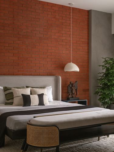 Bedroom with terracotta brick wall, grey upholstered bed, cane bench and hanging dome light
