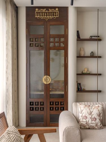 Tall wooden door with ribbed glass panels and rows of brass bells beside floating wood shelves