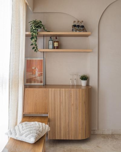 Fluted wood bar cabinet with floating shelves in an arched beige niche, styled with plants and glassware