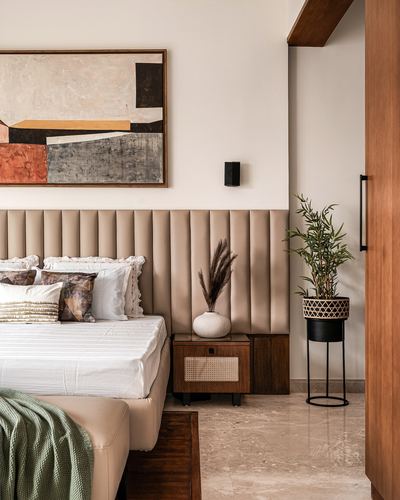 Bedroom with channel-tufted leather headboard, cane nightstand, abstract art, and marble floor