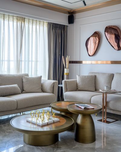 Living room with beige sofas, brass round coffee tables, marble floor and copper wall sculptures