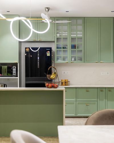 Sage green modular kitchen with island, fluted glass cabinets, and looped pendant light