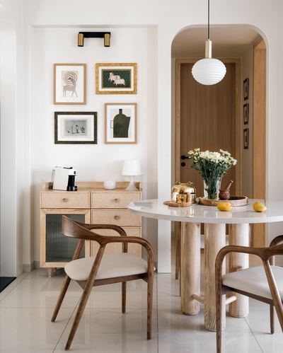 Dining nook with round marble-top table, cane sideboard, and gallery wall in Ahmedabad home