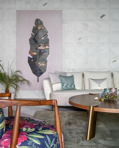 Living room corner with paneled marble wall, leaf art panel, cream sofa, cane-armed chair, round wood coffee table
