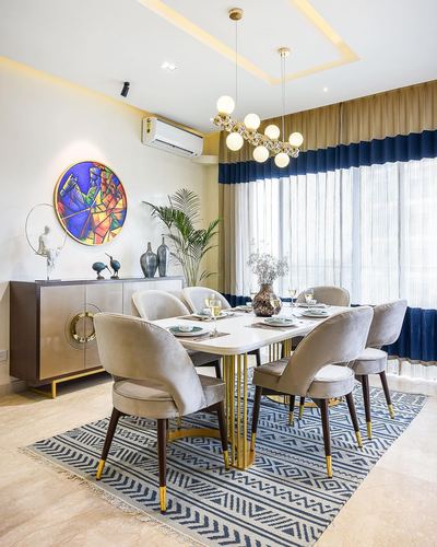 Dining room with marble table, grey velvet chairs, gold chandelier, navy curtains and colorful round wall art