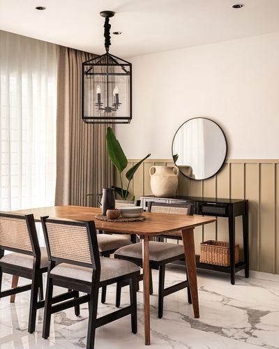 Dining table with cane chairs beneath lantern pendant, olive paneled wall with round mirror behind