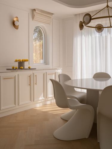 Cream dining room with arched window, curved white chairs around oval table, brass sconce, herringbone floor