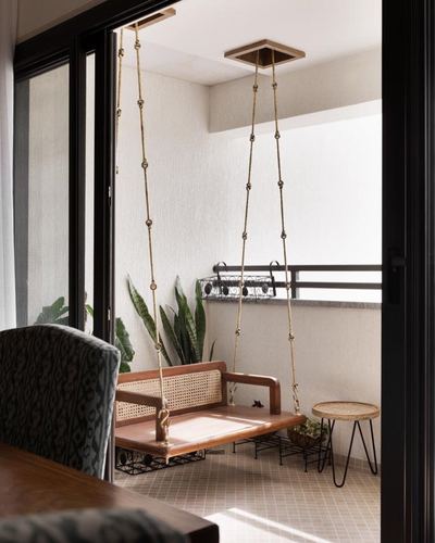 Cane wood swing hanging from beaded chains on a sunlit balcony seen through glass doors