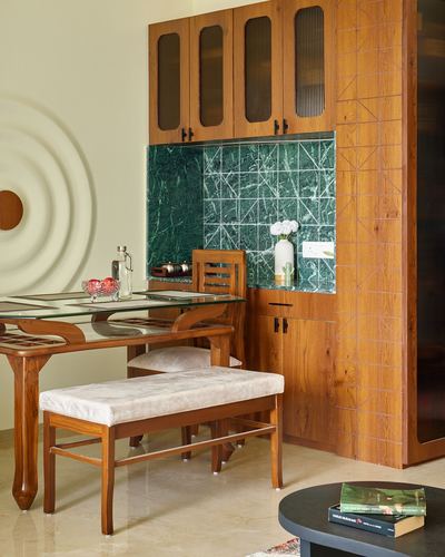 Wooden dining nook with glass-top table, cushioned bench and green stone backsplash cabinet