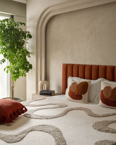 Bedroom with terracotta channel headboard, arched plaster wall detail, and swirl-patterned rug