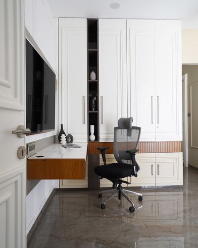 White paneled study nook with floating wood desk, wall tv, and mesh office chair on polished stone floor