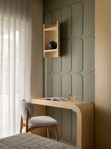 Curved wood desk with boucle chair against a fluted sage green panelled wall beside sheer curtains