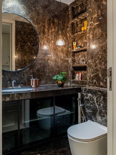 Dark veined stone bathroom with round mirror, pendant light, and wall-mounted toilet