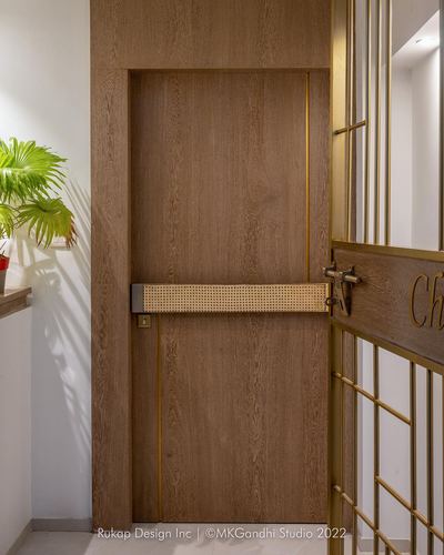 Wooden entrance door with brass trim and horizontal cane inlay, beside a brass grille gate