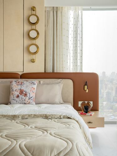 Bedroom corner with tan leather headboard, brass wall sconce, and city view through sheer curtains