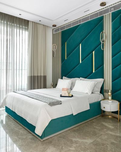Bedroom with teal diagonal-tufted velvet headboard wall, white bedding, round nightstand and marble floor