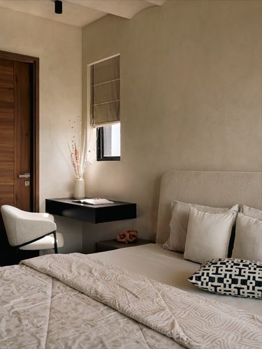 Neutral bedroom with limewashed walls, upholstered headboard, and a small floating desk by the window