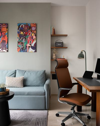 Home office corner with brown ergonomic chair, wooden desk, and blue sofa beside colorful pop art