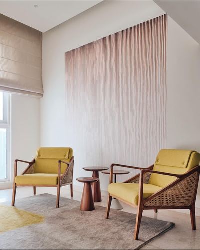 Two mustard cane-and-wood armchairs flank nesting wooden side tables before a ribbed wood feature wall