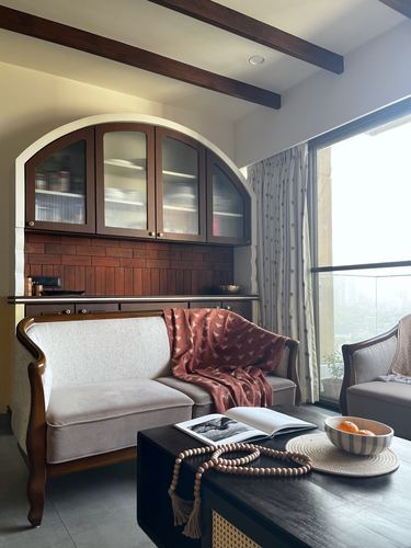 Living room with arched terracotta cabinet, wood beams, cane loveseat, and city view window