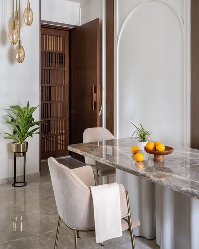 Dining nook with marble table, beige boucle chairs and arched wall niche beside slatted wooden door