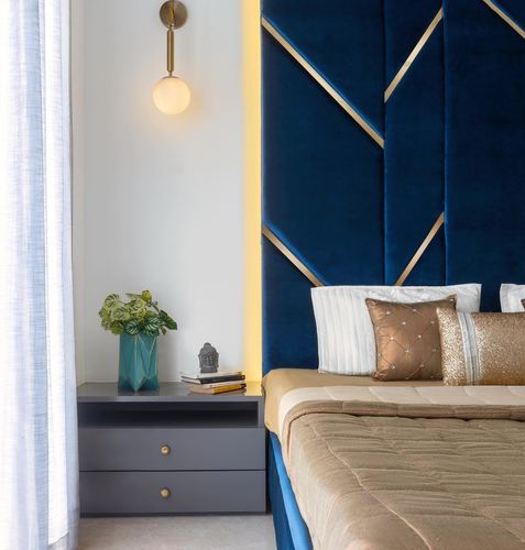 Navy velvet geometric headboard with gold trim beside a grey nightstand and globe sconce