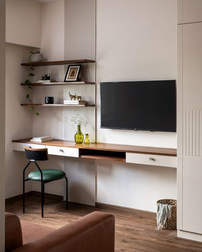 Study nook with floating wood desk, open shelves, wall-mounted TV, green leather chair, fluted panelling