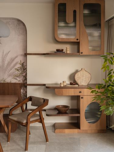 Wooden dining nook with sculpted shelving, ceramics, cane armchair, and mural wall