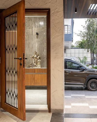 Open teak door with jali grille reveals foyer with brass Krishna statue on stone wall