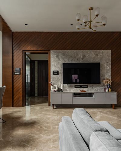 Living room with diagonal wood-panelled wall, stone tv backdrop, and brass chandelier