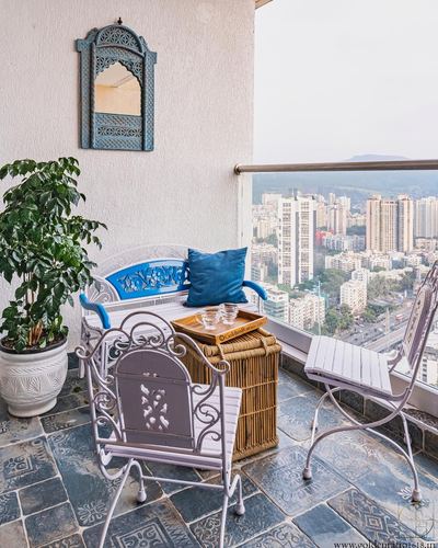 Balcony seating with wicker trunk table, wrought iron chairs, carved mirror, city skyline view