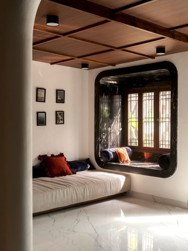Curved white room with wood-paneled ceiling and a dark stone-framed window seat lit by sunlight