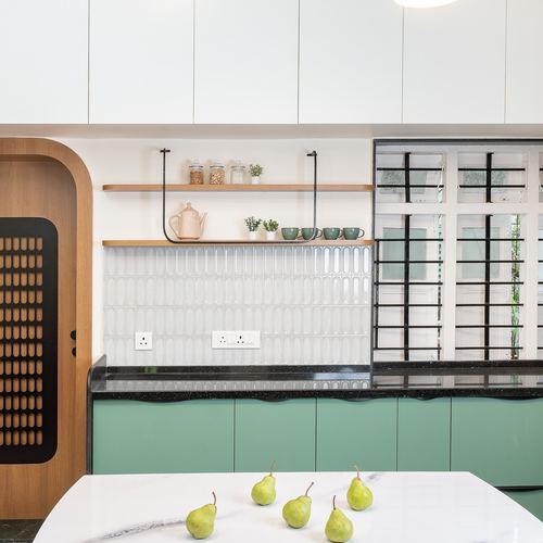 Sage green kitchen cabinetry with black countertop, open wood shelves, and perforated wooden door