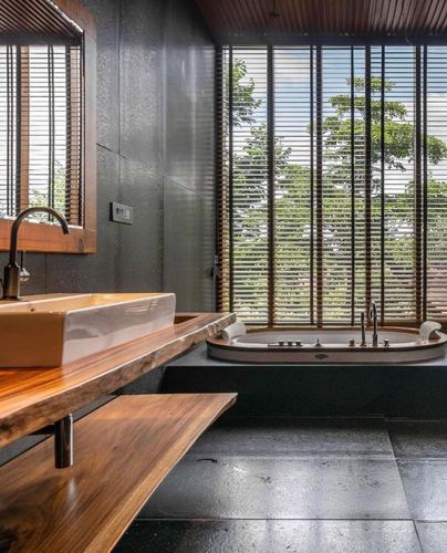 Bathroom with wood vessel sink counter and freestanding tub facing louvered window wall with greenery
