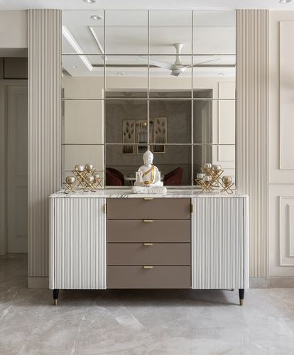 Fluted sideboard with marble top and buddha statue beneath a paneled mirror wall