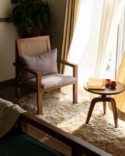 Cane-backed wooden armchair with lavender cushion beside a round side table in sunlit corner
