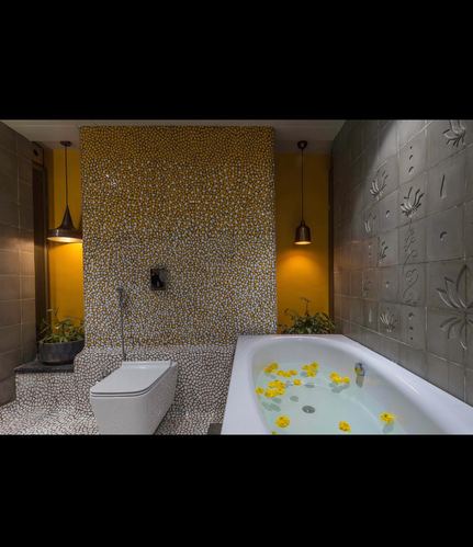 Bathroom with yellow mosaic wall, floating toilet, carved stone panel, and bathtub with floating petals