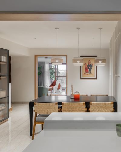 Dining area with black table, cane chairs, three pendant lights, and living room glimpsed beyond