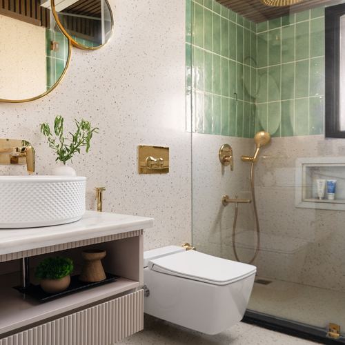 Bathroom with terrazzo walls, green tiled shower, brass fixtures, and round mirror