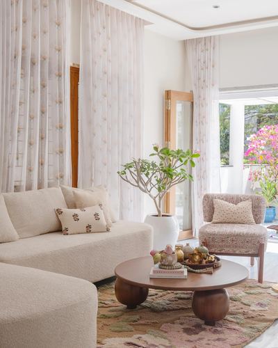 Living room with boucle sofa, round wood coffee table, floral armchair and sheer curtains facing garden