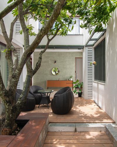 Shaded courtyard deck with black wicker chairs beneath a tree, wall mirror and orange sideboard behind