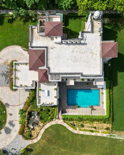 Aerial view of a large farmhouse with pitched red-tiled roofs, a stone terrace, pool, and manicured gardens