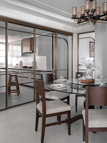 Dining area with round glass table, dark wood chairs, and bronze-framed glass partition to kitchen
