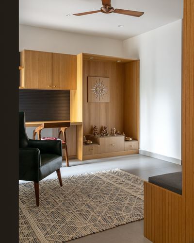 Wood-panelled pooja niche with brass idols beside a study desk and black leather chair