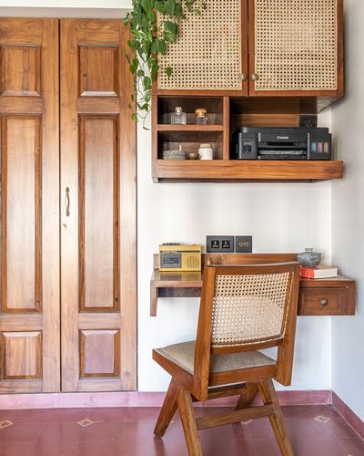 Wooden study nook with cane cabinet, floating desk, printer and cane-backed chair beside wardrobe doors