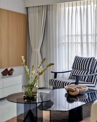 Living room corner with striped armchair, glass coffee table, sheer curtains and wood-panel wall