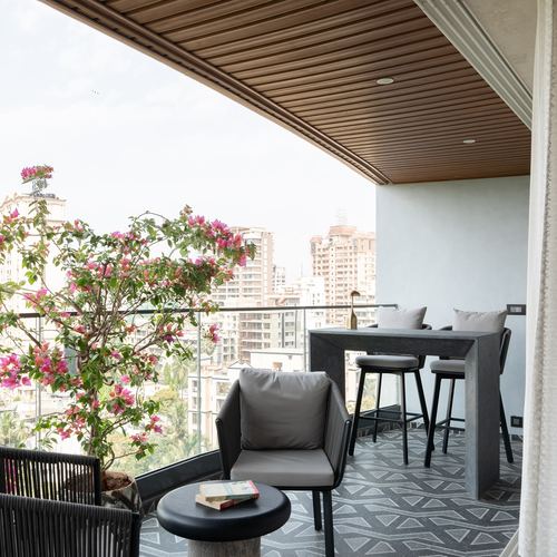 High-rise balcony with wood slat ceiling, dark bar table, stools, and bougainvillea overlooking Mumbai skyline