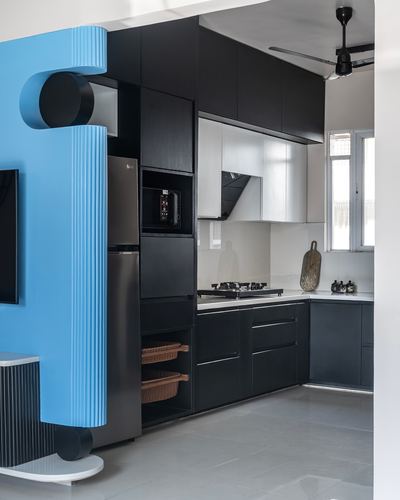 Black modular kitchen with sculptural blue fluted column at entrance, Nashik apartment