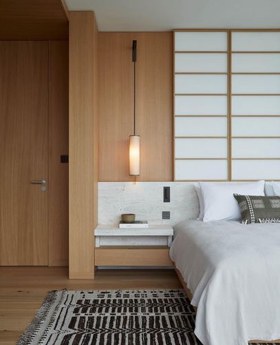 Bedroom with wood paneling, shoji screen, floating stone nightstand and pendant light beside bed
