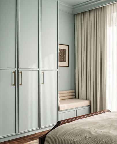 Sage green paneled wardrobe beside a cushioned window seat with beige curtains in a bedroom